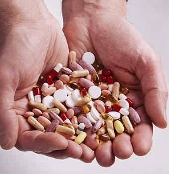 A pair of hands holding a mixed handful of capsules and tablets